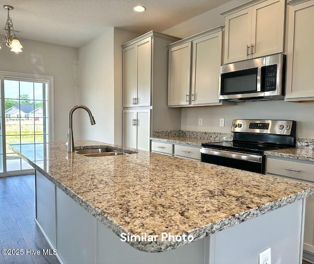 kitchen featuring light stone countertops, sink, hardwood / wood-style floors, decorative light fixtures, and appliances with stainless steel finishes