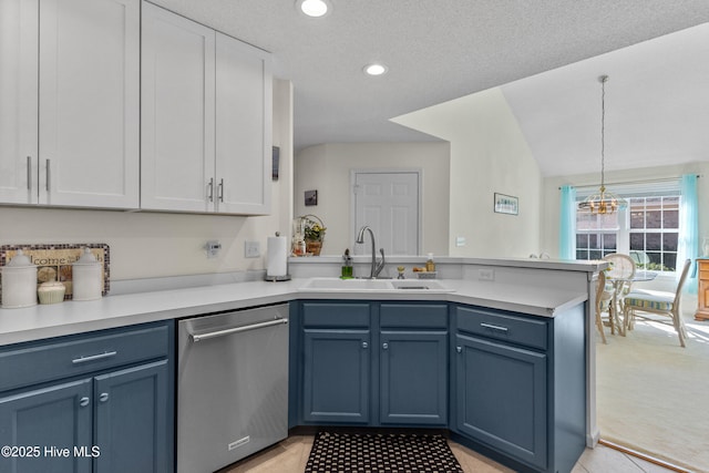 kitchen with blue cabinetry, light countertops, stainless steel dishwasher, a sink, and a peninsula