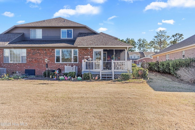 rear view of house featuring a sunroom, a shingled roof, a yard, and brick siding