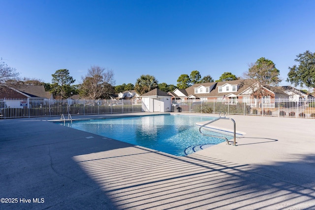 community pool with a patio, an outdoor structure, fence, and a residential view