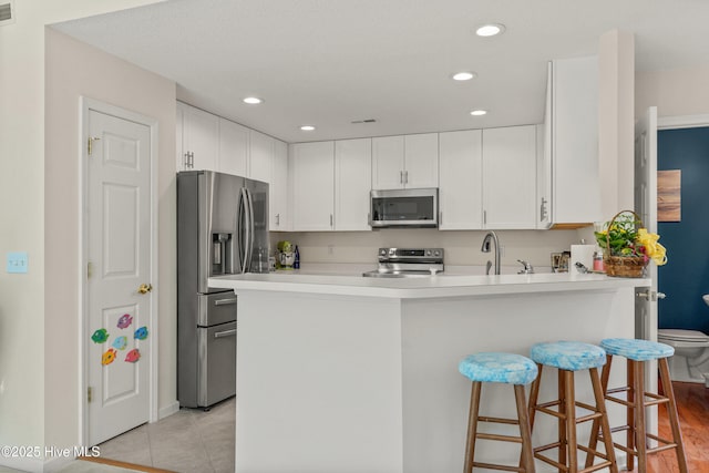 kitchen with a breakfast bar area, a peninsula, white cabinets, light countertops, and appliances with stainless steel finishes