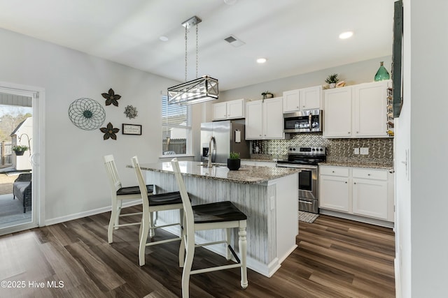 kitchen with a breakfast bar area, white cabinets, light stone counters, and appliances with stainless steel finishes