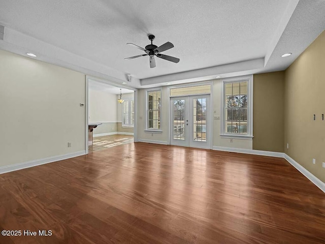 unfurnished living room with hardwood / wood-style floors, ceiling fan, a tray ceiling, a textured ceiling, and french doors