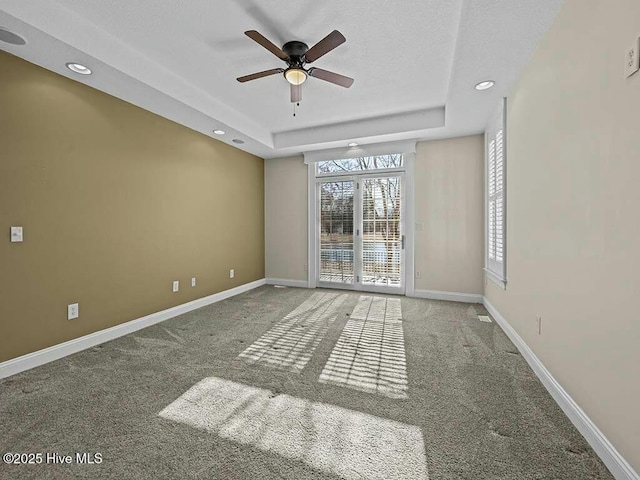 carpeted empty room with ceiling fan and a raised ceiling