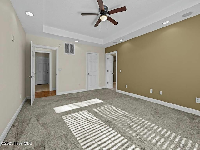 unfurnished bedroom featuring ceiling fan, a raised ceiling, and carpet floors