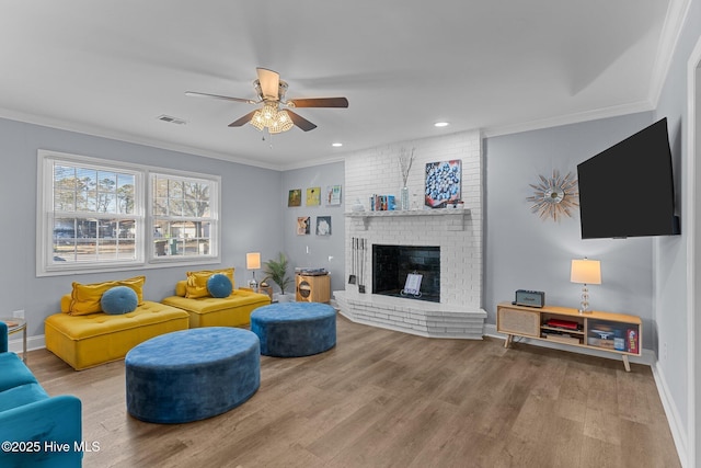 living room featuring crown molding, ceiling fan, a brick fireplace, and hardwood / wood-style flooring