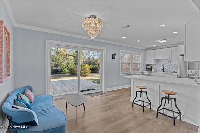 kitchen with stainless steel refrigerator, white cabinets, a kitchen bar, ornamental molding, and light wood-type flooring