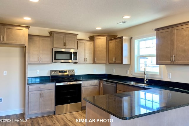 kitchen with sink, light hardwood / wood-style flooring, dark stone countertops, appliances with stainless steel finishes, and kitchen peninsula