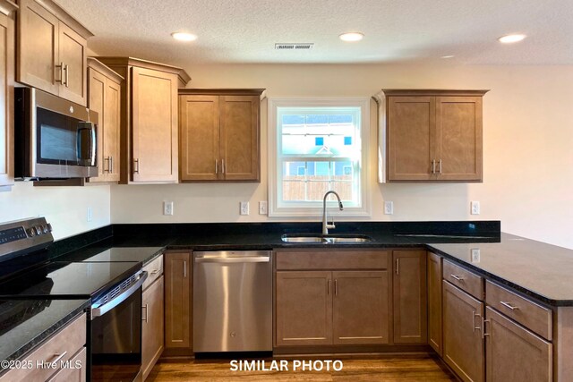 kitchen featuring appliances with stainless steel finishes, a textured ceiling, sink, hardwood / wood-style flooring, and dark stone countertops