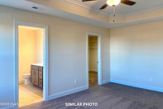 unfurnished bedroom featuring a tray ceiling, ceiling fan, ornamental molding, and ensuite bathroom