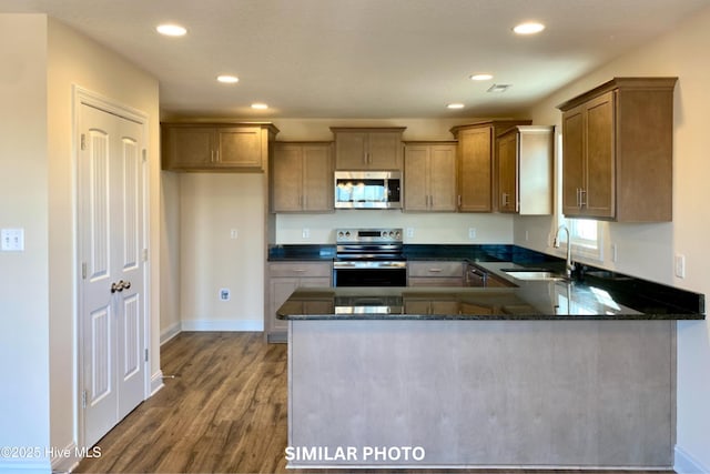 kitchen with kitchen peninsula, appliances with stainless steel finishes, dark stone counters, sink, and wood-type flooring