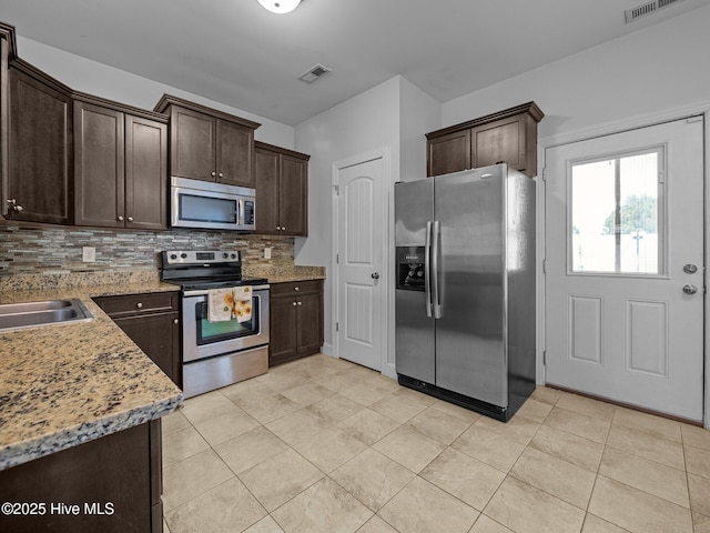 kitchen with light stone countertops, dark brown cabinets, backsplash, and stainless steel appliances