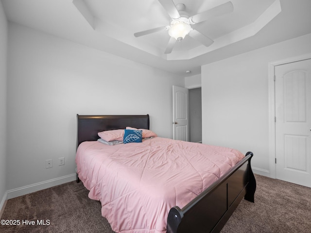 bedroom featuring ceiling fan, dark carpet, and a tray ceiling