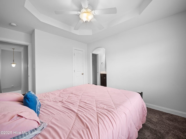 bedroom with dark carpet, ensuite bathroom, ceiling fan, and a raised ceiling