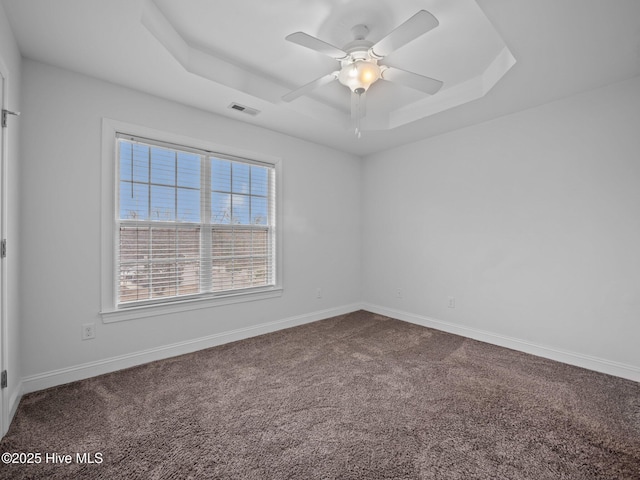 empty room featuring carpet floors, a tray ceiling, and ceiling fan