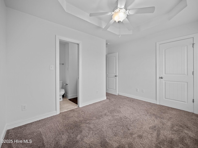 unfurnished bedroom featuring ceiling fan, light carpet, ensuite bath, and a tray ceiling