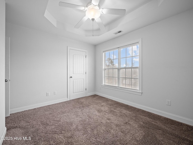 carpeted empty room with ceiling fan and a raised ceiling