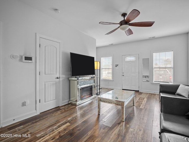 living room featuring ceiling fan, a stone fireplace, and dark wood-type flooring