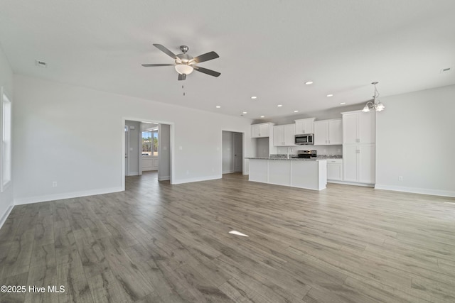 unfurnished living room featuring sink, ceiling fan with notable chandelier, and light hardwood / wood-style floors