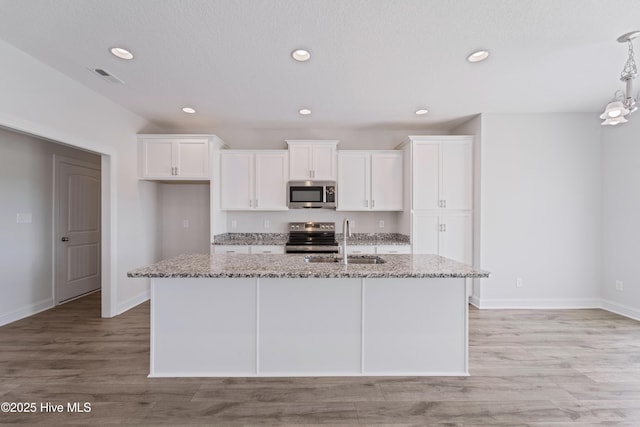 kitchen featuring sink, light stone countertops, an island with sink, and appliances with stainless steel finishes