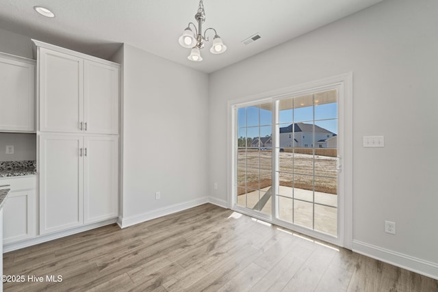 unfurnished dining area with an inviting chandelier and light hardwood / wood-style flooring