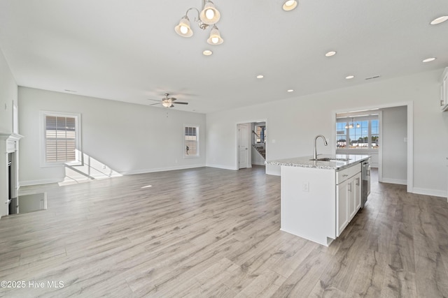 kitchen featuring sink, a center island with sink, light stone countertops, light hardwood / wood-style floors, and white cabinets