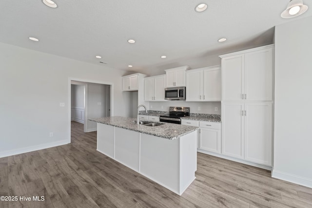 kitchen featuring appliances with stainless steel finishes, white cabinetry, sink, light stone countertops, and a center island with sink