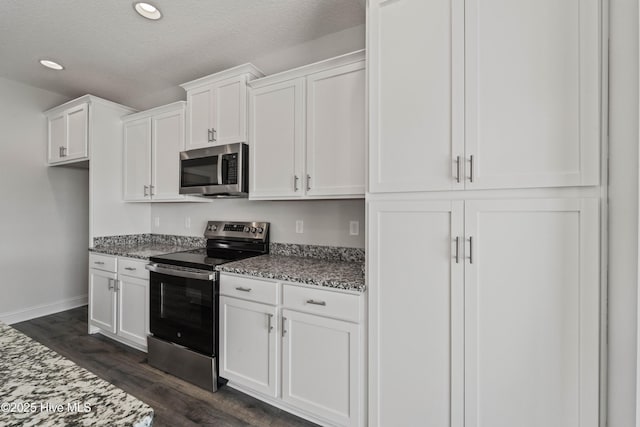 kitchen featuring stainless steel appliances, white cabinetry, dark wood-type flooring, and dark stone countertops