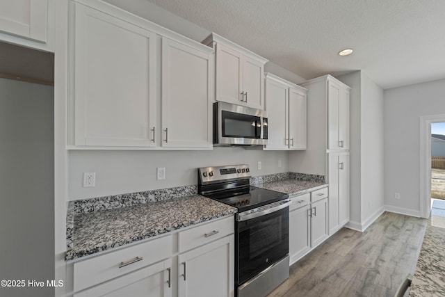 kitchen with white cabinetry, dark stone countertops, light hardwood / wood-style floors, stainless steel appliances, and a textured ceiling