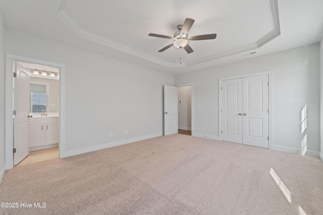 unfurnished bedroom with a raised ceiling, crown molding, light carpet, ensuite bath, and a closet