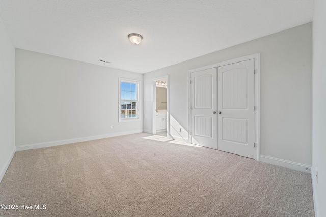 unfurnished bedroom featuring ensuite bath, light colored carpet, and a closet