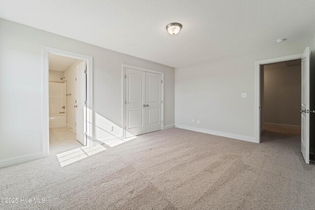 unfurnished bedroom featuring ensuite bathroom, light colored carpet, and a closet