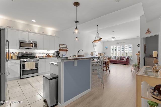 kitchen featuring ceiling fan, stainless steel appliances, white cabinetry, and a kitchen breakfast bar