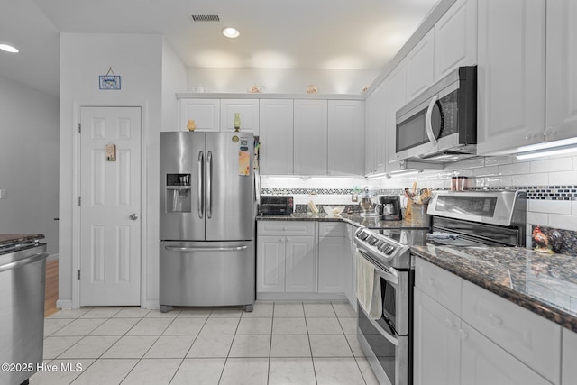 kitchen featuring appliances with stainless steel finishes, dark stone countertops, light tile patterned floors, and white cabinetry