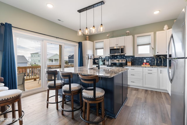 kitchen featuring white cabinetry, stainless steel appliances, and an island with sink