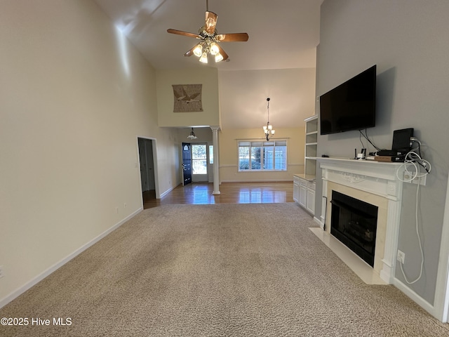 unfurnished living room featuring ceiling fan, light carpet, a high ceiling, a fireplace with flush hearth, and baseboards