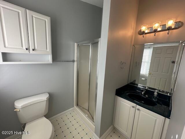 bathroom with toilet, a stall shower, baseboards, and vanity