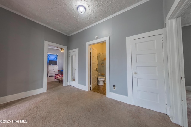 unfurnished bedroom featuring a textured ceiling, ensuite bathroom, a closet, crown molding, and carpet flooring