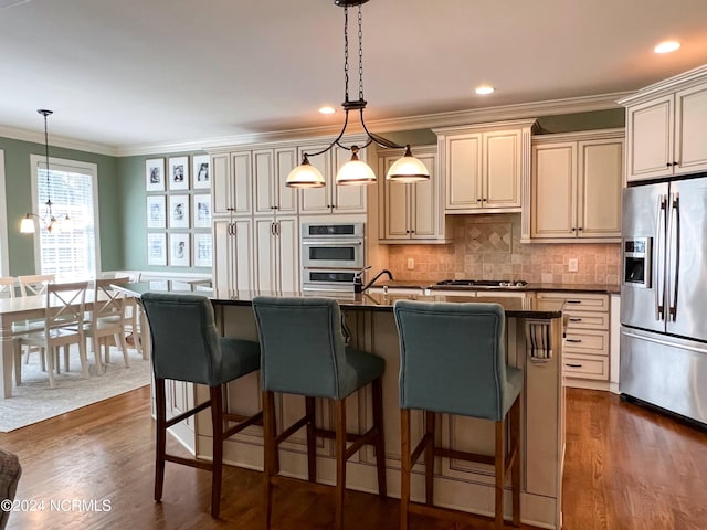 kitchen with tasteful backsplash, stainless steel appliances, a kitchen island with sink, cream cabinets, and decorative light fixtures