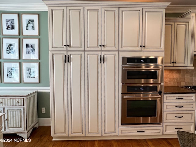 kitchen featuring dark stone counters, ornamental molding, double oven, tasteful backsplash, and dark hardwood / wood-style flooring