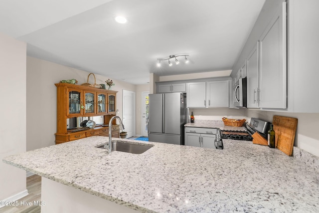 kitchen with light stone counters, gray cabinets, a sink, a peninsula, and appliances with stainless steel finishes