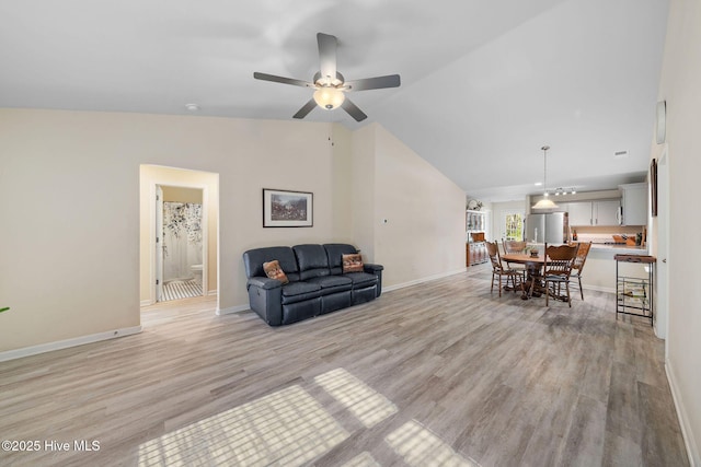 living area featuring vaulted ceiling, baseboards, a ceiling fan, and light wood-style flooring