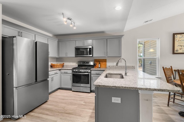 kitchen featuring kitchen peninsula, light stone countertops, stainless steel appliances, gray cabinets, and sink