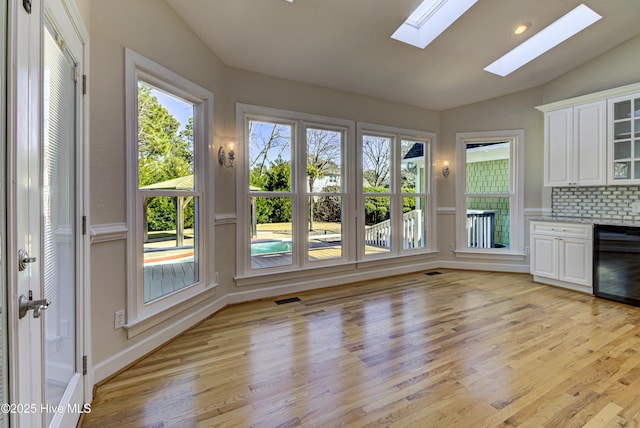 interior space with vaulted ceiling with skylight, light hardwood / wood-style floors, decorative backsplash, black dishwasher, and white cabinets