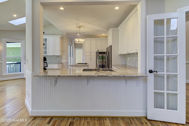 kitchen featuring vaulted ceiling with skylight, white cabinets, double oven, tasteful backsplash, and hanging light fixtures