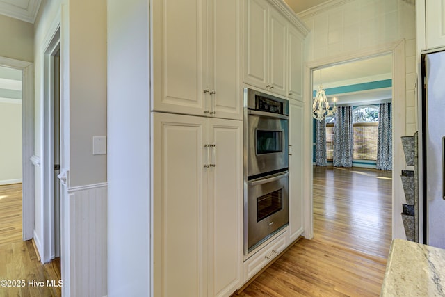 kitchen with decorative light fixtures, light stone countertops, crown molding, double oven, and light hardwood / wood-style flooring