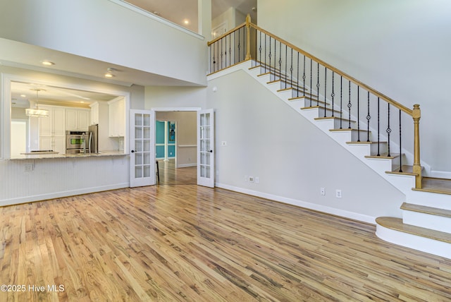 unfurnished living room featuring a high ceiling, light hardwood / wood-style floors, and french doors