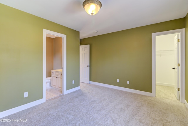 unfurnished bedroom featuring light carpet, a closet, a walk in closet, and ensuite bath