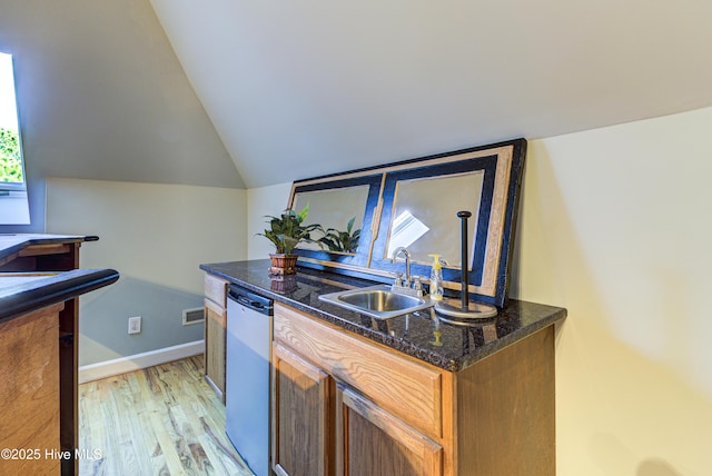 kitchen with vaulted ceiling, dark stone countertops, light hardwood / wood-style floors, stainless steel dishwasher, and sink