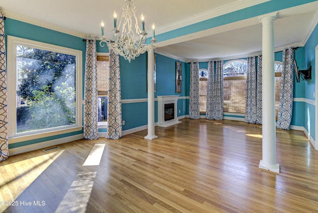 unfurnished dining area with ornate columns, hardwood / wood-style floors, ornamental molding, and a chandelier